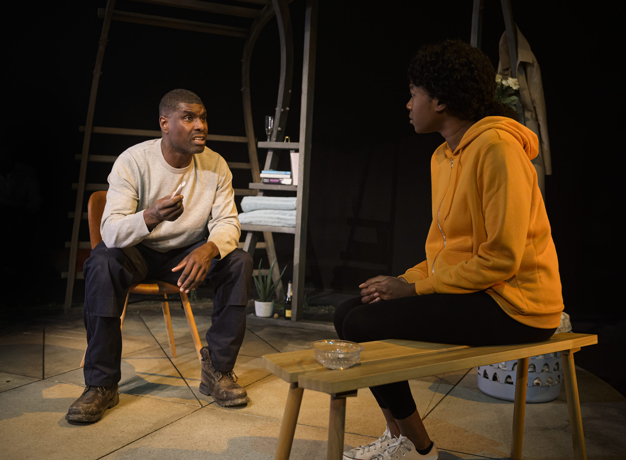 Two black performers, Evlyne Oyedokun and Stanley J Browne, sit together on stage, deep in conversation.