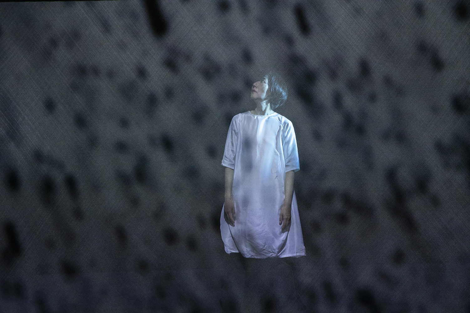 Thumbnail image for the 'Case study film: Chisato Minamimura' video. Chisato stands on stage in a long white t-shirt type dress. There is a hazy film over the lense of the camera so it looks like Chisato is standing in a snow storm or a thick fog.