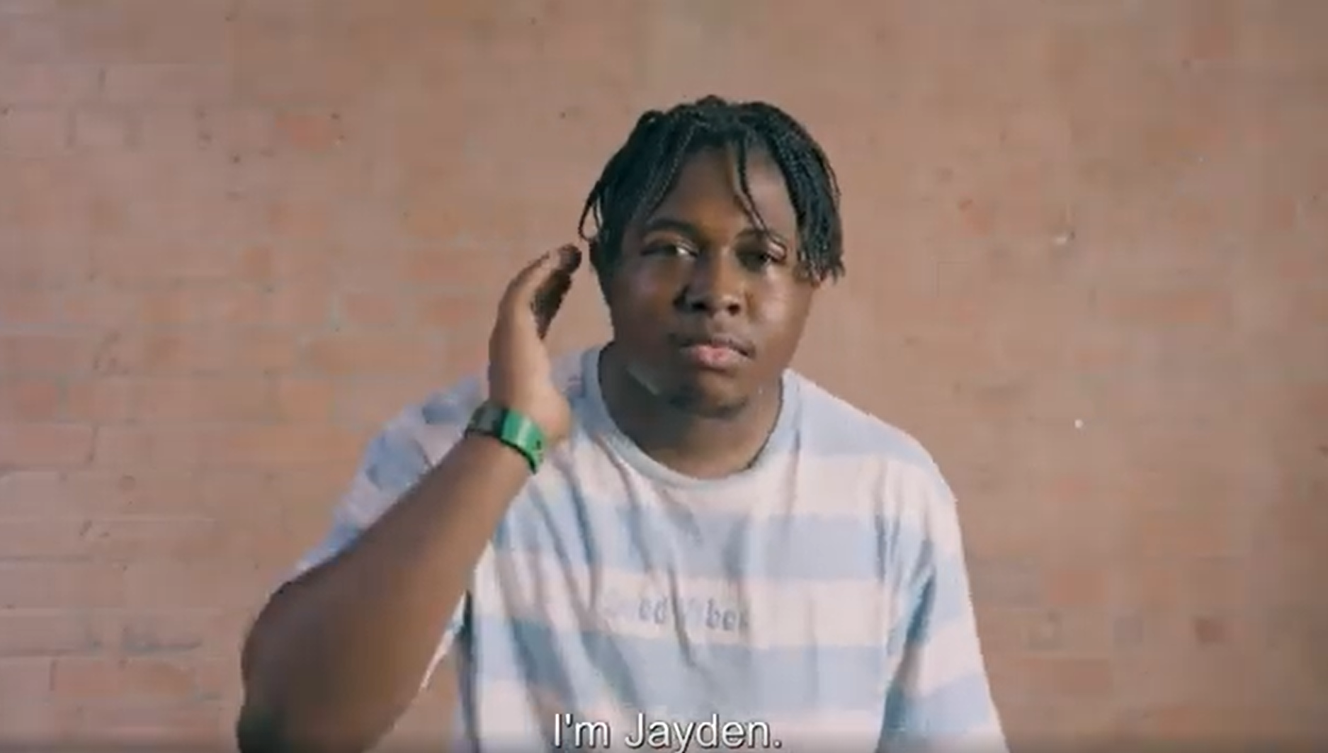 A young black man wearing a blue and white striped shirt signing.