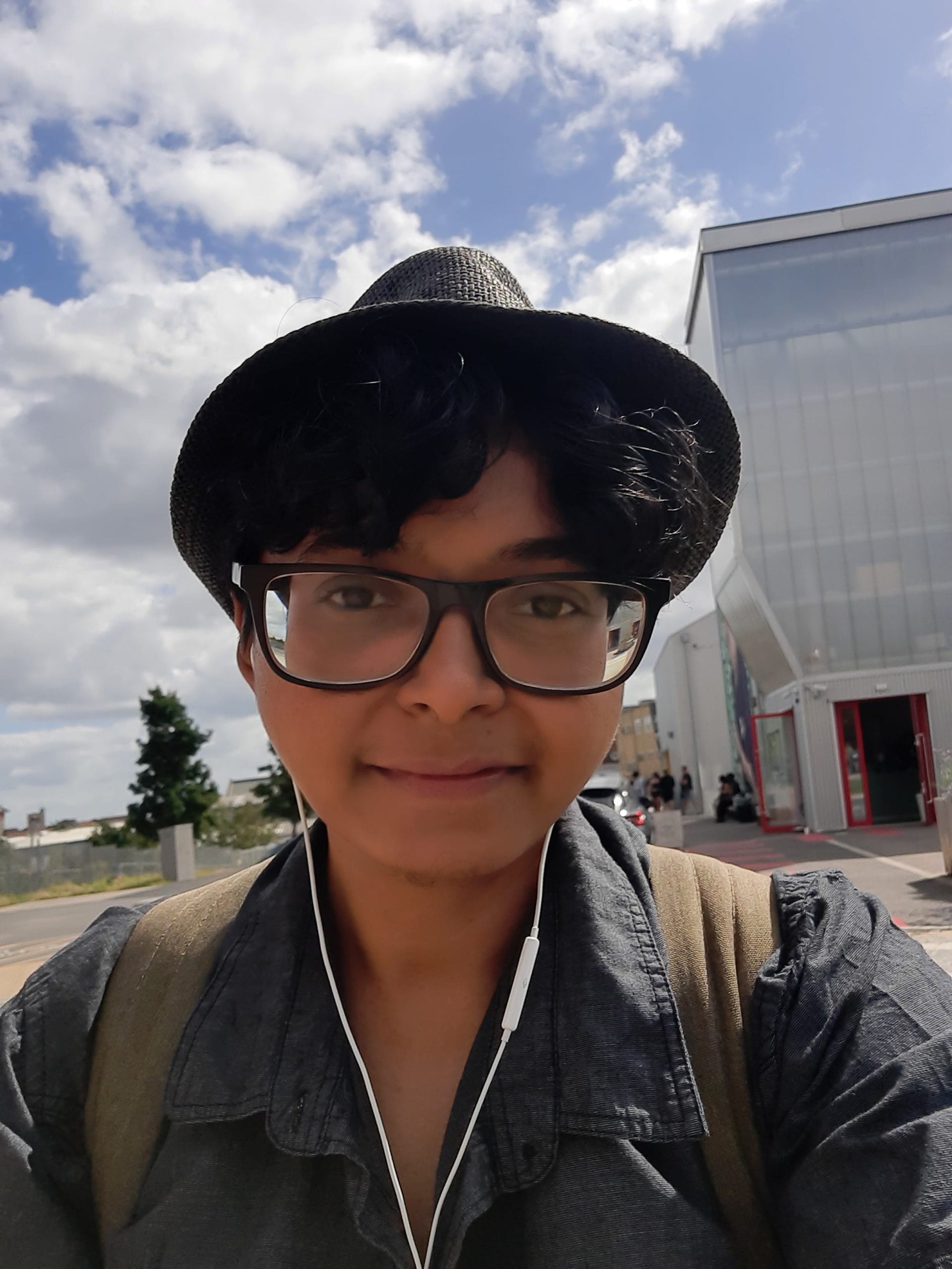 Manishta has short, curly dark hair and is wearing a red and black striped top. Xe have brown skin, and is looking directly at the camera.